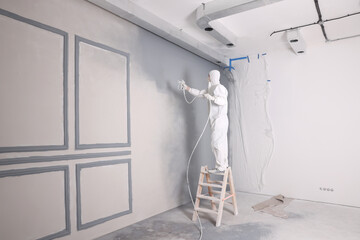 Decorator dyeing wall in grey color with spray paint indoors