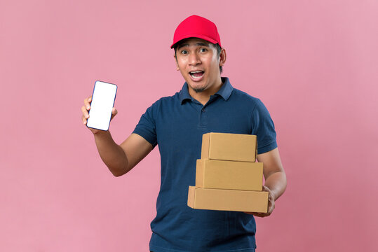 Happy young delivery man showing phone screen in red cap holding parcel post box