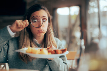 Funny Food Critic Checking the Restaurant Dish with a Magnifying Glass. Picky eater analyzing the...
