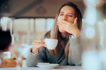 Sleepy Woman Having a Coffee at the Restaurant. Yawning girl addicted to caffeine in need for her...