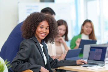Happy beautiful Asian businesswoman sitting smiling and enjoying working on laptop in office and looking at camera.