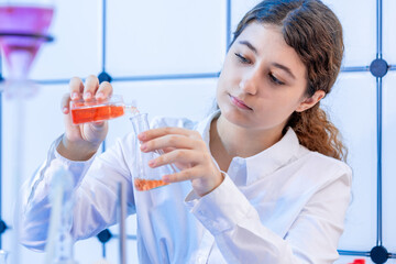 young woman in a microbiology laboratory fills a cell culture flask with a nutrient solution from a test tube