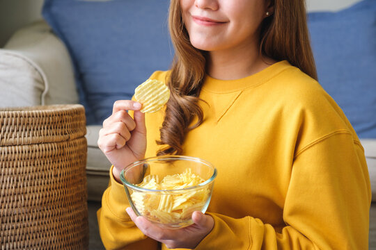 Closeup image of a young woman picking and eating potato chips at home