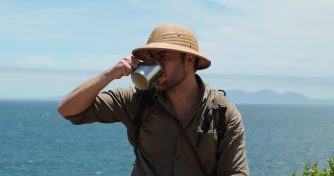 Hikers sit on top of rock, take pictures with camera, drink hot coffee from thermos flask. tourist with a backpack resting. male traveler in safari sun hat drinking hot drink from iron tourist cup