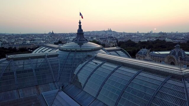 Still aerial shot of Paris city at dawn, featuring glass roof of famous Tourist attraction, the Grand Palais with french flag waving on the top of dome.