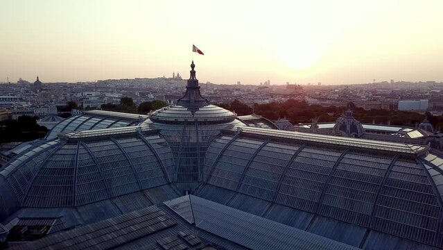 Aerial Revealing shot of Grand palais with french flag on top, highlighting Pairs city at sunrise with Petit palais along.