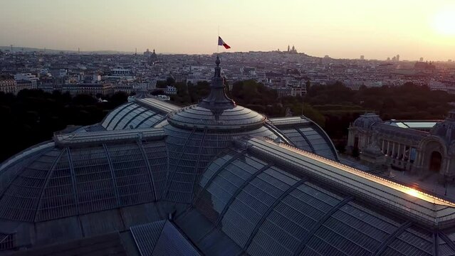 A beautiful sunrise at The Grand palais captured by orbiting drone in Paris City with a French flag waiving on the top of iconic building 