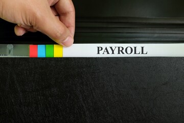 Hand picking payroll file in black binder folder. Human resources and accounting management concept.