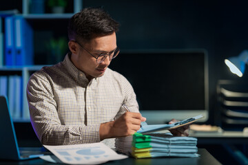 Overtime work concept, Handsome asian business man working late at night in office workplace.