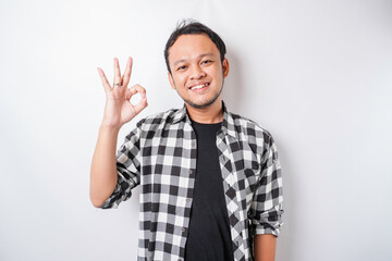 Fototapeta premium Excited Asian man wearing tartan shirt giving an OK hand gesture isolated by a white background