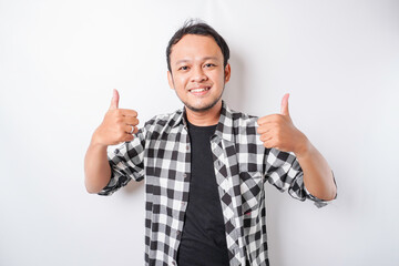 Excited Asian man wearing tartan shirt gives thumbs up hand gesture of approval, isolated by white background