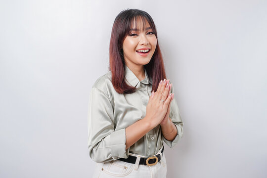 Smiling young Asian woman wearing sage green shirt, gesturing traditional greeting isolated over white background