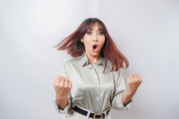 A young Asian woman with a happy successful expression wearing sage green shirt isolated by white background