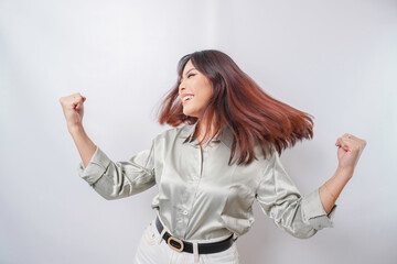 A young Asian woman with a happy successful expression wearing sage green shirt isolated by white background