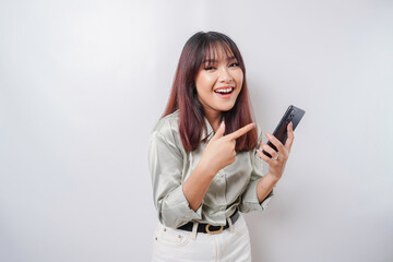Fototapeta premium A portrait of a happy Asian woman wearing a sage green shirt and holding her phone, isolated by white background