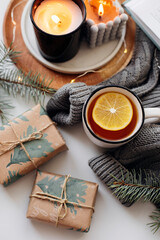 Top view on cup with tea, warm sweater, candles, present gifts and fir tree. Winter home cozy concept