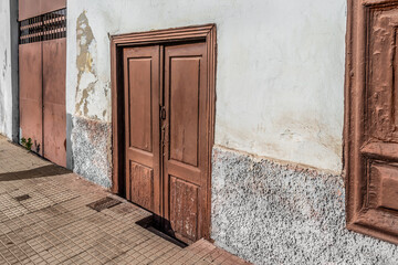 White shabby wall and old wooden doors of a building on Calle Afilarmonica Nifu-Nifa street in Santa Cruz de Tenerife, Spain. Vintage architecture of the Canary Islands