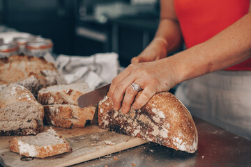 Woman cutting a loaf of freshly baked wholemeal sourdough bread.