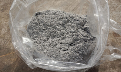 Gray ashes in a plastic bag placed on a wooden floor for use as a fertilizer for plants growing in an agricultural garden.