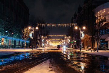 Fototapeta na wymiar winter night on christmas decoration lighting street of town during melted snowfall precipitation