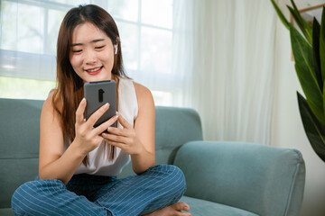 Happy beautiful woman relaxation she shopping online with smartphone, Smiling Asian female sitting on sofa talking mobile smart phone at living room at home, Social media networks communication