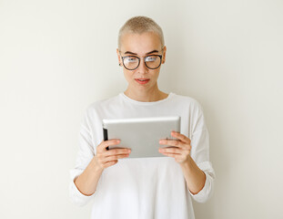 Beautiful woman freelancer with very short hair holding tablet and looking at camera on blank wall