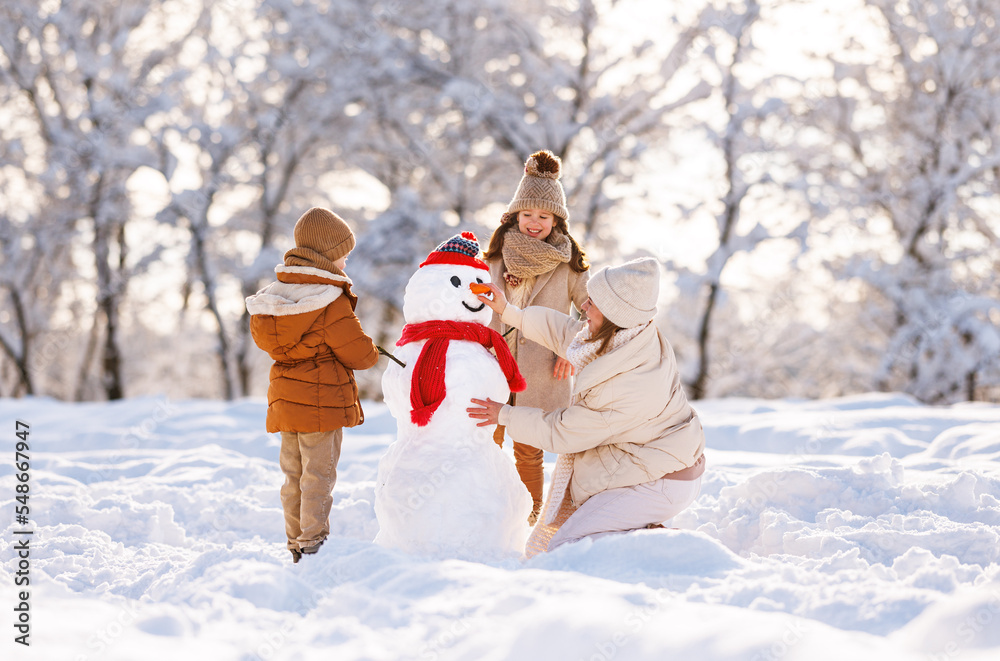 Sticker happy family mother and two little kids making snowman together in winter park outdoors