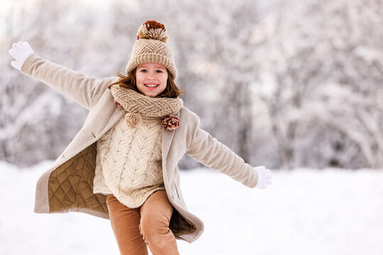 Happy excited little girl playing in winter park, kid running through snow with arms outstretched