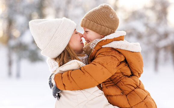 Happy family enjoying snowy weather outdoor, mom with little son hugging during walk in winter park