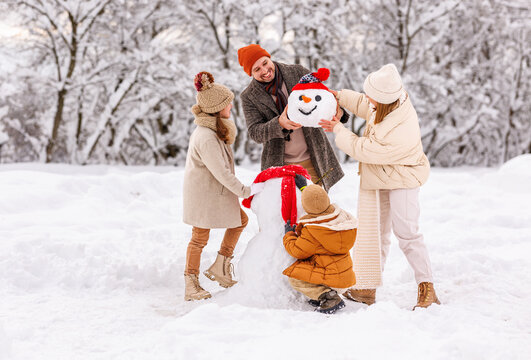 Happy children sculpting funny snowman together with parents in winter snow-covered park
