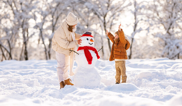 Cute little boy making snowman with mom in winter park