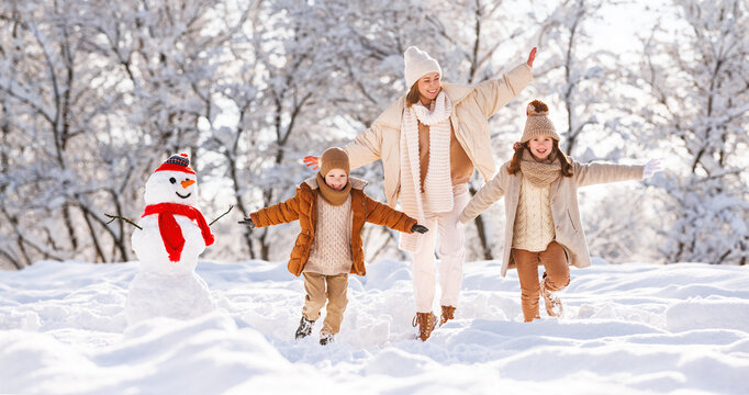 Young positive family mother and two little kids joyfully running through white snow in winter park