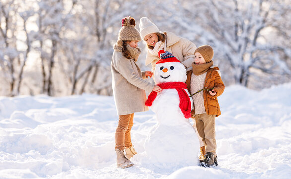 Happy family mother and two little kids making snowman together in winter park outdoors