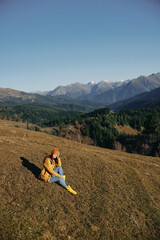 Woman sitting full-length on a hill and looking out over the mountains happy nature trip on a hike in the autumn