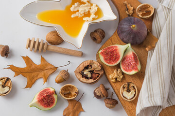 Fototapeta na wymiar Autumn still-life with ripe figs cut in slices, walnuts and plate full of honey on wooden cutting board. Healthy snacks.