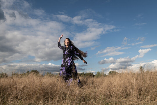 portrait of happy smiling asian woman in classic dress dancing in field outside under blue sky