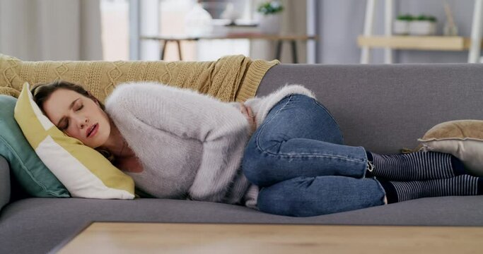 Period pain, holding stomach and woman on sofa lying down to rest, recover and relax after cramps. Health, menstruation and girl suffering from bloating, menstrual and abdomen pain hug belly on couch