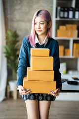 Young Asian SMEs woman holding parcels, standing among several boxes in modern office.