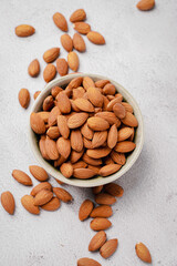 Almonds in white porcelain bowl on white table. Almond concept with copyspace.