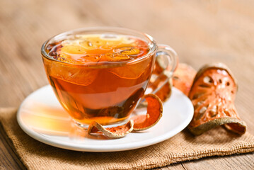 Bael tea on glass with dried bael slices on wooden background, Bael  juice - Dry bael fruit tea for health - Aegle marmelos