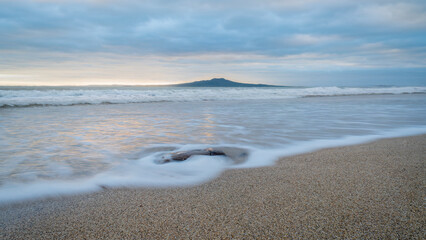Sunrise at Rangitoto Island, slow movement of sea waves at foreground, Milford beach, Auckland.