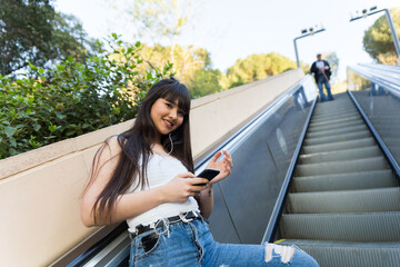 Asian european woman going on a stairways while she listen to music with her phone and headphones, in the natural light of the streets of Barcelona