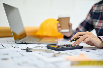 Engineer or architect working on blueprint, using calculator and sipping coffee. cropped image