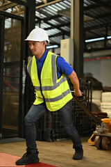 Determined Asian male warehouse worker concentrating on pulling the pallet truck with parcel