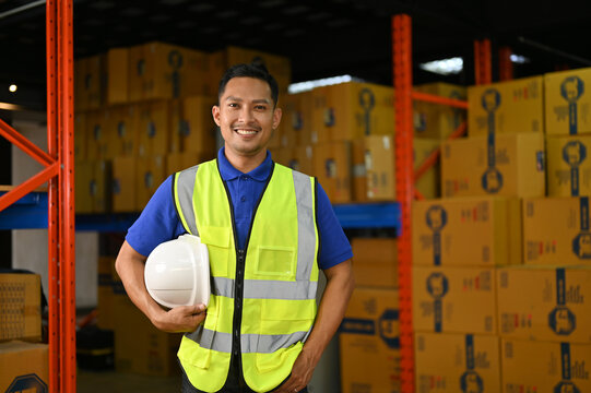 Smart Asian male factory engineer or warehouse supervisor in uniform holding his hardhat