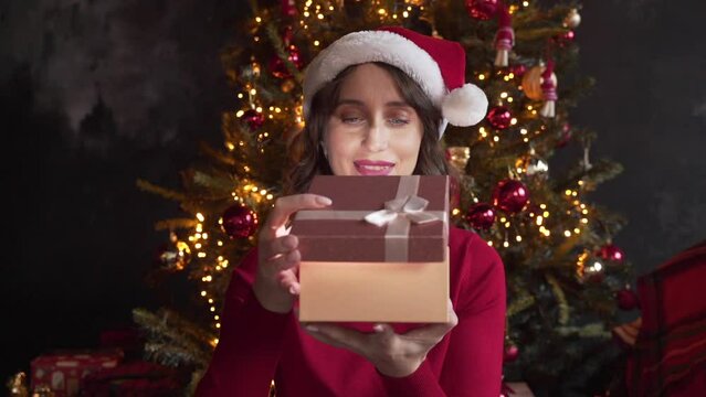 A young beautiful woman is opening a gift box, light shines on her face. 