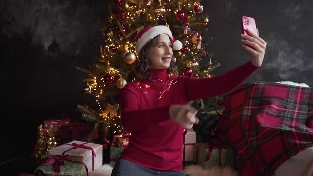 White woman in red sweater holds smart phone make video call on Christmas Eve 