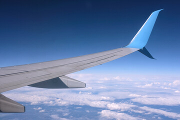 View from the high flying passenger plane to the wing and calm white clouds on blue sky