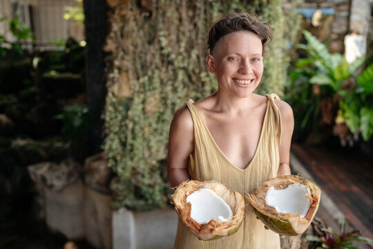 Portrait of a beautiful young woman with a smile. In the hands of halves of fresh coconut for wellness treatments. Useful natural products for body and organism.