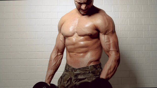 Side view of muscular topless bodybuilder who pumping biceps with dumbbells over white background